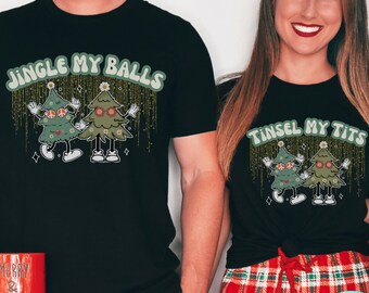 May include: A black t-shirt with the text "Jingle My Balls" and a cartoon image of two Christmas trees with faces and peace signs. The trees are wearing sunglasses and have glitter falling from them. The shirt is paired with red and green plaid pyjama trousers.