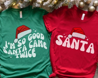 Può includere: Due magliette a tema natalizio. Una maglietta verde con testo bianco che recita "I'm so good Santa came twice" e un'immagine di cappello di Babbo Natale rosso. L'altra maglietta è rossa con testo bianco che recita "SANTA" e un'immagine di cappello di Babbo Natale rosso.