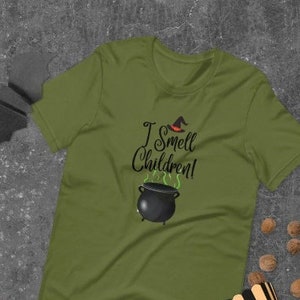 May include: Olive green t-shirt with the text "I Smell Children!" above a black cauldron with green steam. A witch's hat is above the cauldron. The shirt is a Halloween-themed graphic tee.