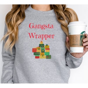 Puede incluir: Sudadera gris con el texto "Gangsta Wrapper" en rojo y un gráfico de una pila de regalos envueltos.