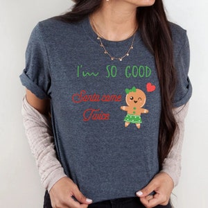 May include: A dark heather grey t-shirt with the text "I'm so good Santa came twice" in red and green lettering. A cartoon gingerbread girl with a green skirt and a red heart is also on the shirt.