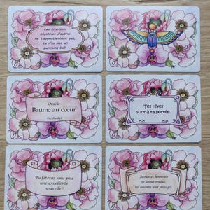 May include: Set of 6 oracle cards with pink floral designs and inspirational messages. The cards feature a white background with a scroll-like banner containing the message. The messages are: "Les &eacute;motions n&eacute;gatives d'autrui ne t'appartiennent pas, tu n'es pas un punching-ball.", "Oracle Baume au c&oelig;ur Par Aurliel", "Tes r&ecirc;ves sont &agrave; ta port&eacute;e.", "Tu f&ecirc;teras sous peu une excellente nouvelle!", "Justice et honneurs te seront rendus, tes int&eacute;r&ecirc;ts sont prot&eacute;g&eacute;s."