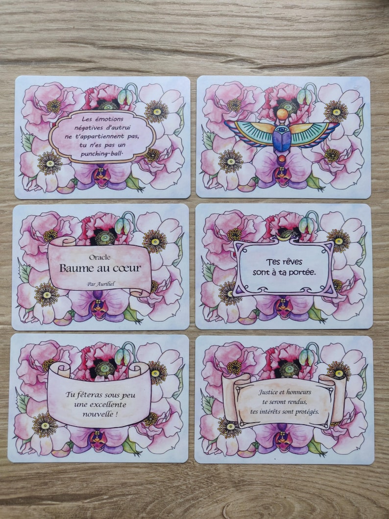 May include: Set of 6 oracle cards with pink floral designs and inspirational messages. The cards feature a white background with a scroll-like banner containing the message. The messages are: "Les &eacute;motions n&eacute;gatives d'autrui ne t'appartiennent pas, tu n'es pas un punching-ball.", "Oracle Baume au c&oelig;ur Par Aurliel", "Tes r&ecirc;ves sont &agrave; ta port&eacute;e.", "Tu f&ecirc;teras sous peu une excellente nouvelle!", "Justice et honneurs te seront rendus, tes int&eacute;r&ecirc;ts sont prot&eacute;g&eacute;s."