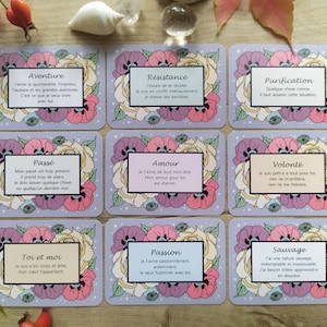 May include: A set of 10 cards with floral designs and inspirational quotes in French. Each card features a different quote about love, adventure, resistance, purification, the past, and more. The cards are printed on a light purple background with white stars.