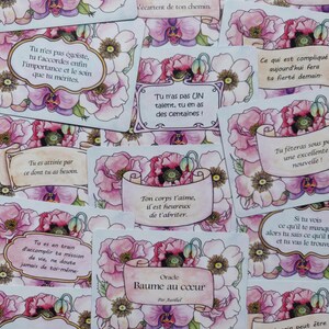 May include: A set of oracle cards with floral illustrations and inspirational messages. The cards are white with pink and purple flowers and have a light blue background. The text on the cards is in French. The cards are titled "Baume au c&oelig;ur" and "Oracle".