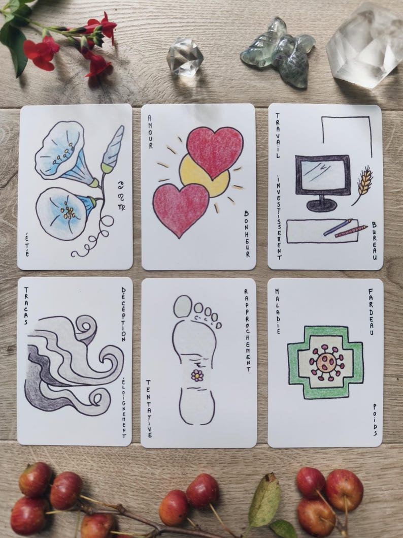 May include: Six illustrated tarot cards with hand-drawn images and French text. The cards feature images of flowers, hearts, a foot, and a computer. The cards are arranged on a wooden surface with crystals and flowers.