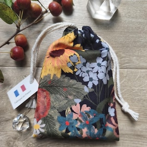 May include: A drawstring pouch with a floral pattern featuring sunflowers, daisies, and other flowers in yellow, blue, and pink. The pouch has a white drawstring closure and a tag that says "Fabriqu&eacute; en France."