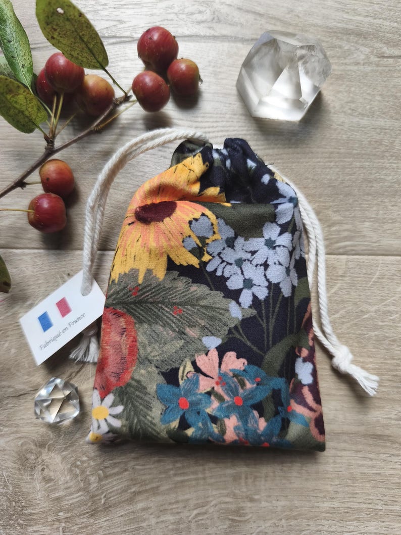 May include: A drawstring pouch with a floral pattern featuring sunflowers, daisies, and other flowers in yellow, blue, and pink. The pouch has a white drawstring closure and a tag that says "Fabriqu&eacute; en France."