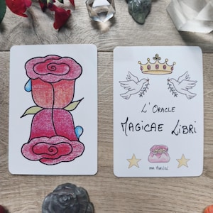 May include: Two tarot cards with illustrations of a rose and doves with a crown. The card on the left features a red rose with blue teardrops. The card on the right has the text "L'Oracle Magicae Libri" and illustrations of doves, a crown, and stars.