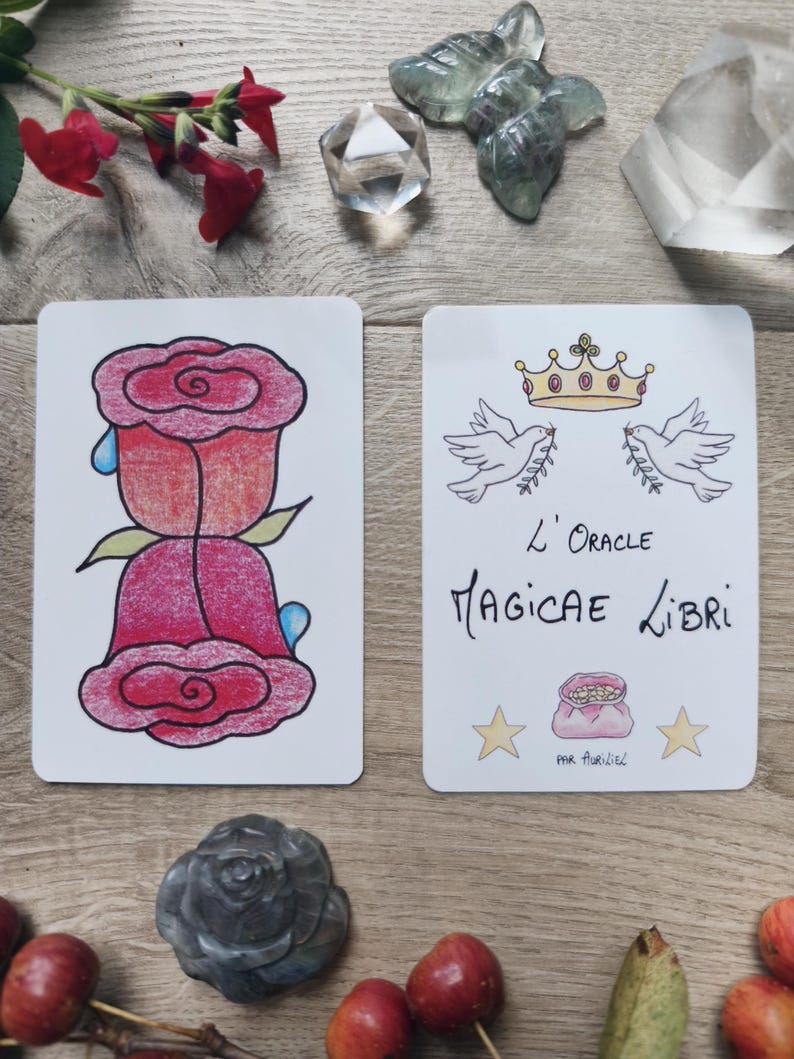 May include: Two tarot cards with illustrations of a rose and doves with a crown. The card on the left features a red rose with blue teardrops. The card on the right has the text "L'Oracle Magicae Libri" and illustrations of doves, a crown, and stars.