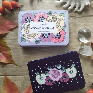 May include: Two oracle cards with floral designs. The top card is light purple with white stars and features a bouquet of pink, white, and purple flowers. The text on the card reads "Oracle coeur &agrave; coeur Aurelie Millaret". The bottom card is dark purple with white stars and features a bouquet of pink, white, and green flowers.