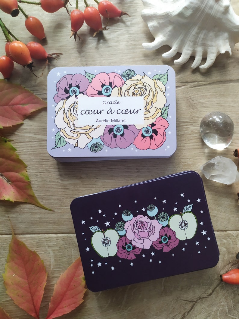 May include: Two oracle cards with floral designs. The top card is light purple with white stars and features a bouquet of pink, white, and purple flowers. The text on the card reads "Oracle coeur &agrave; coeur Aurelie Millaret". The bottom card is dark purple with white stars and features a bouquet of pink, white, and green flowers.