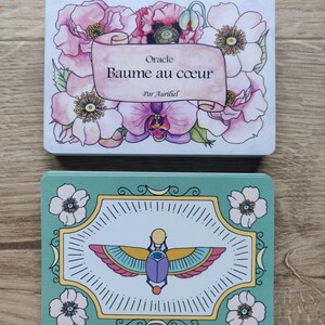 May include: Two oracle cards with floral designs. The top card is white with pink and purple flowers and the text "Oracle Baume au coeur Par Auriel". The bottom card is green with a white background and a colorful scarab beetle design.