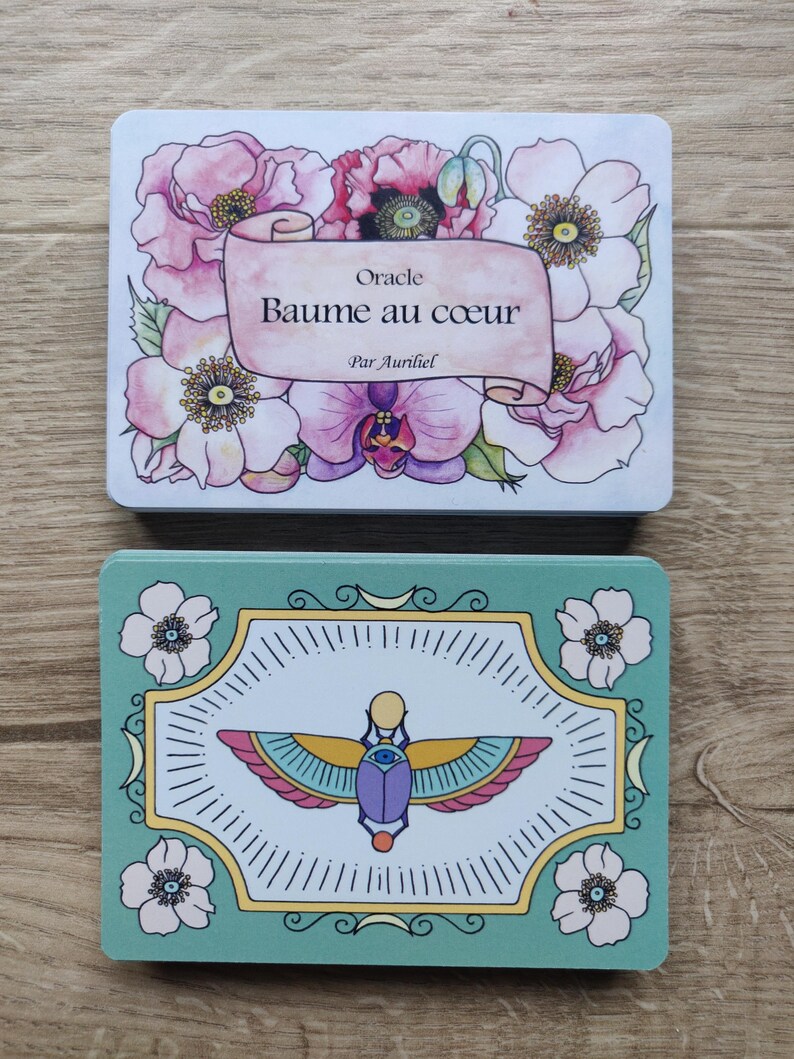May include: Two oracle cards with floral designs. The top card is white with pink and purple flowers and the text "Oracle Baume au coeur Par Auriel". The bottom card is green with a white background and a colorful scarab beetle design.