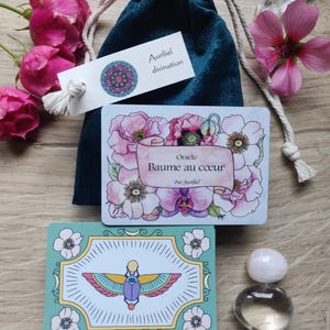 May include: A teal velvet bag with a white tag that reads "Auriel divination" and a card with a floral design and the text "Oracle Baume au coeur Par Auriel".