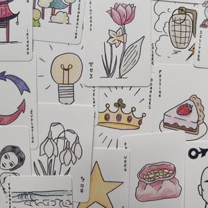 May include: A selection of illustrated cards with drawings and text. The cards depict a lightbulb, a flower, a crown, and a slice of cake. Text includes words like "Spring", "Evolution", and "Passion".