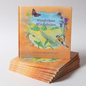 Può includere: Una pila di libri illustrati per bambini con una copertina gialla. La copertina presenta un uccello, una farfalla e fiori. Il titolo del libro è "Wunderbare Winzigkeiten" e il sottotitolo è "Ein Spaziergang durchs Jahr".