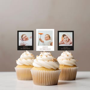 May include: Three cupcakes with white frosting and gold sprinkles are in front of three small framed photos of a baby. The photos have the text "Jack's 1st Birthday". The baby is in different poses in each photo.