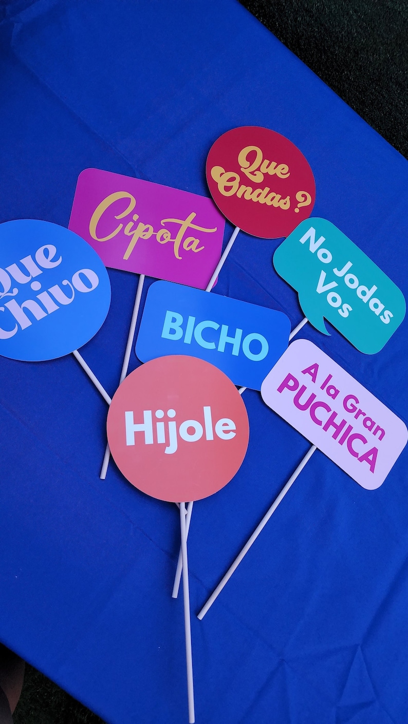 May include: A set of colorful cardboard signs with Spanish phrases, including "Que Ondas?", "Cipota", "Que Chivo", "No Jodas Vos", "Bicho", "Hijole", and "A la Gran Puchica".