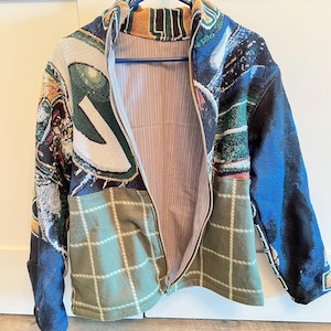 Könnte beinhalten: Mehrfarbige Jacke mit Reißverschluss und Patchwork-Design. Die Jacke weist eine Mischung aus Mustern auf, darunter Karomuster, abstrakte Kunst und einfarbige blaue Ärmel. Das Innenfutter ist ein hellrosa und weiß gestreifter Stoff.