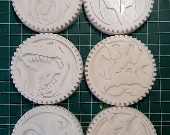 May include: Six white plastic round medallions with different embossed designs. The medallions have a raised edge and a textured surface.