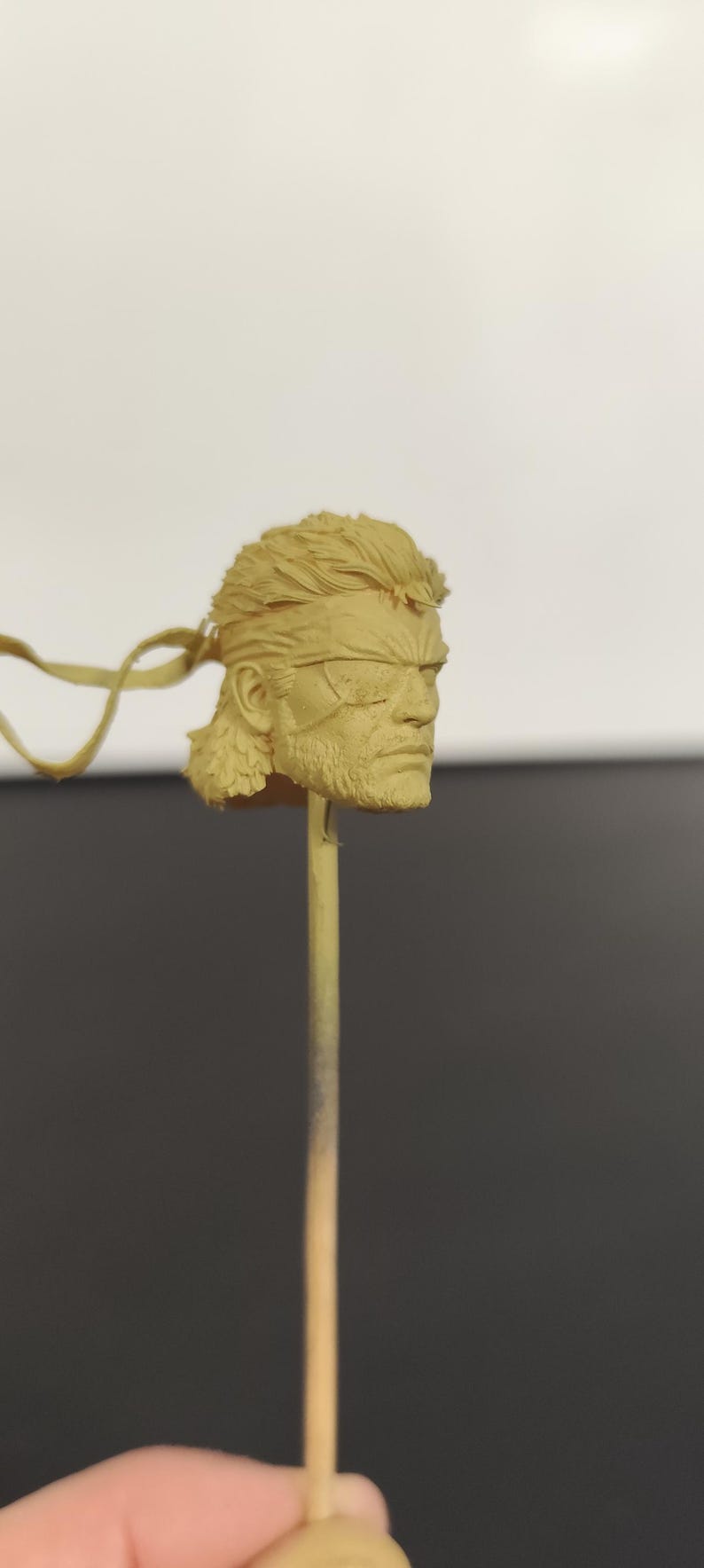 Peut inclure: Une sculpture de t&ecirc;te en r&eacute;sine non peinte de couleur beige repr&eacute;sentant un personnage avec une coiffure courte et textur&eacute;e, une barbe prononc&eacute;e et un cache-&oelig;il sur l'&oelig;il gauche. La t&ecirc;te est fix&eacute;e sur une fine tige verticale pour la peinture.
