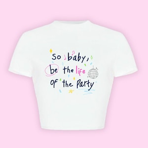 Könnte beinhalten: Weißes Crop-Top mit dem Schriftzug "so baby, be the life of the Party" in farbenfrohem, handschriftlichem Stil. Das Design umfasst eine Discokugel, Noten und Sterne.