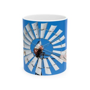 May include: A white windmill with wooden blades against a bright blue sky. The windmill has a red metal gear and a sign that reads "Agern Ranch" in white letters.