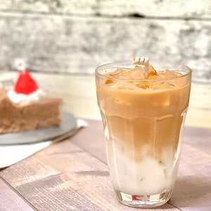 May include: A glass of iced coffee with milk and ice cubes. The coffee is a light brown color and the milk is white. The glass is clear and has a rounded bottom.