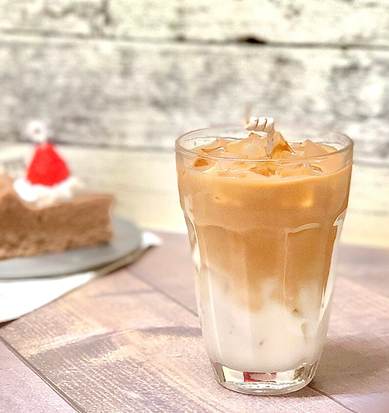 May include: A glass of iced coffee with milk and ice cubes. The coffee is a light brown color and the milk is white. The glass is clear and has a rounded bottom.