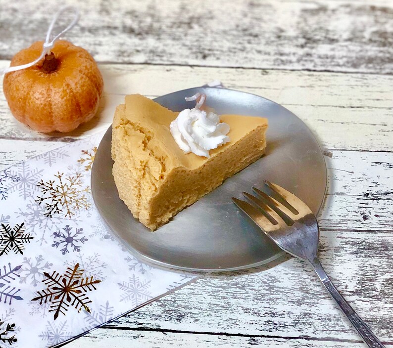 May include: A slice of pumpkin cheesecake with whipped cream on top, on a silver plate with a fork beside it.
