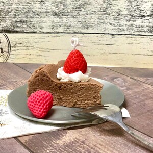 May include: A slice of chocolate cheesecake topped with whipped cream and a red strawberry. The cheesecake is on a silver plate with a fork.