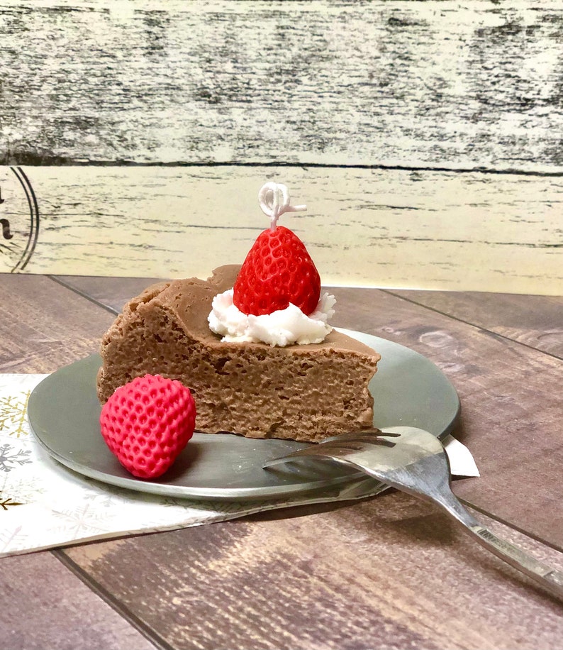 May include: A slice of chocolate cheesecake topped with whipped cream and a red strawberry. The cheesecake is on a silver plate with a fork.