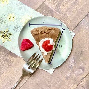May include: A slice of chocolate cake with whipped cream and a strawberry on top, on a light blue plate with a fork. The cake is 2 inches wide and 3.5 inches long.