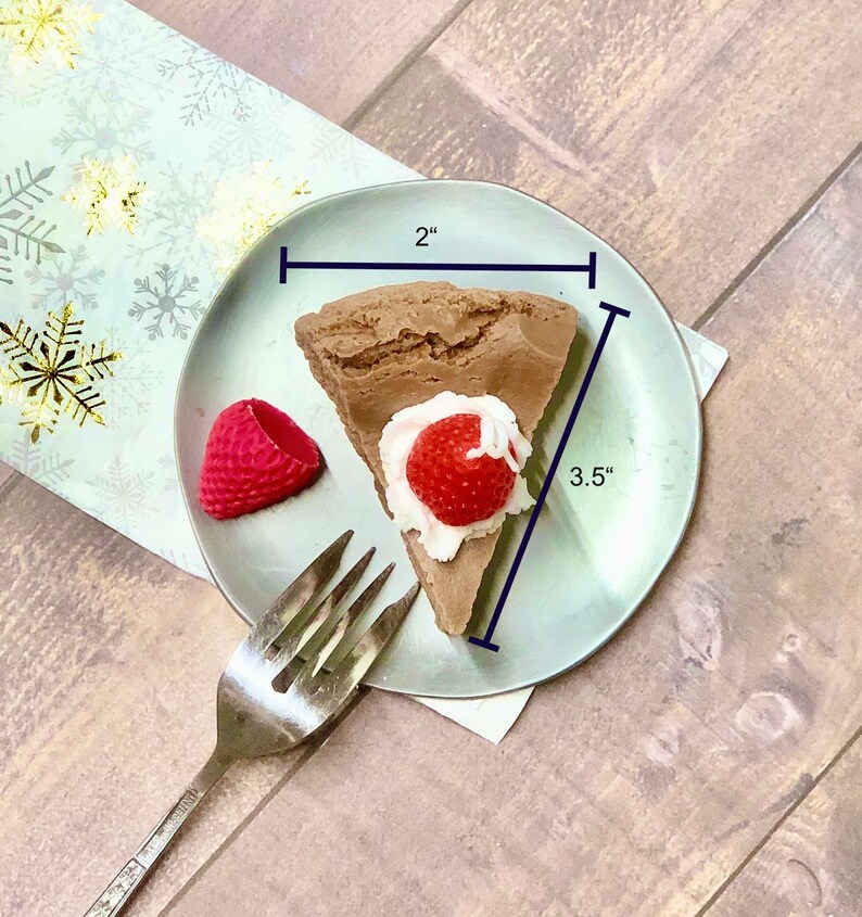 May include: A slice of chocolate cake with whipped cream and a strawberry on top, on a light blue plate with a fork. The cake is 2 inches wide and 3.5 inches long.