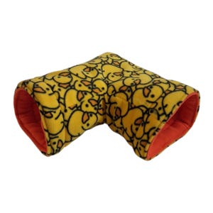 May include: A yellow fleece pet tunnel featuring a pattern of cartoon duck faces. The interior is bright orange. The tunnel is bent at a 90-degree angle.