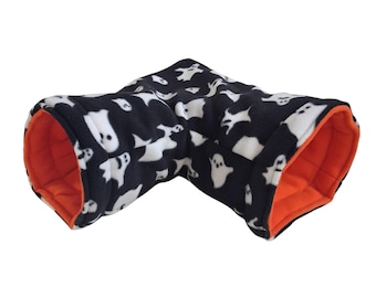 May include: An L-shaped pet tunnel featuring a black exterior with a white ghost pattern and a solid orange interior lining. The tunnel is constructed from a soft, plush fabric and has two open ends for entry and exit.