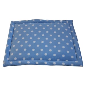 May include: A rectangular pet bed with a light blue background and white polka dots. The bed has a padded border in a matching light blue color. The soft, plush material is designed for comfort.