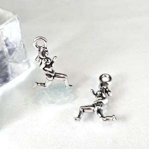 May include: Two silver charms depicting a kneeling figure. Each charm has a loop at the top for attaching to a chain. The charms are on a white surface.