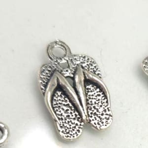 May include: A silver-colored flip-flop charm with textured details. The charm features a loop at the top for easy attachment. The flip-flop design is a popular symbol of summer and beach themes.