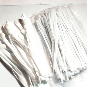 May include: A collection of white elastic cords with adjustable white plastic beads. Some cords are bundled together, while others are in a clear plastic bag. The cords are likely for face masks or other craft projects.