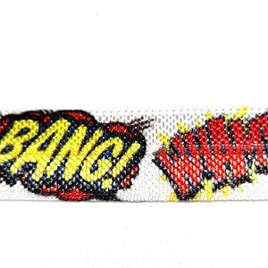 May include: White ribbon featuring comic book-style text bubbles with the words "BANG!" and "POW!" in bold, colorful fonts. The text is outlined in black and filled with yellow, red, and blue. The ribbon is suitable for crafts.