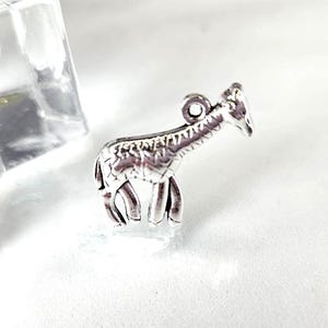 May include: A small, silver-colored giraffe charm with detailed markings. The charm has a loop at the top for attaching to a necklace or bracelet. The giraffe is standing, with its head and neck extended.
