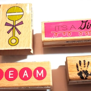 Sellos de goma con temática de bebé e inspiración: sonajero para bebé (5 x 5 cm), palabra "Sueño" (2,5 x 7,6 cm), ¡Es niña! (2,5 x 7,6 cm), huellas de manos de bebé (2,5 x 5 cm) usadas.