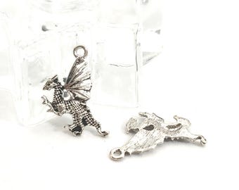 May include: Two silver-colored dragon charms. One dragon is upright with detailed wings and a loop for hanging. The other charm is a flat, detailed dragon. Both charms are on a white surface.
