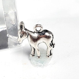 May include: A small, silver-colored donkey charm with a loop for attaching to a necklace or bracelet. The donkey is standing, with its head turned slightly to the left. The charm is detailed with visible ears, eyes, and legs.