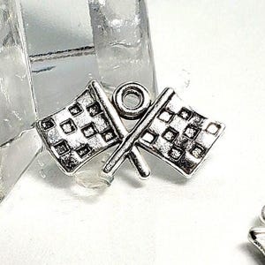 May include: Silver-toned charm featuring two crossed checkered racing flags. The flags have a detailed square pattern and are connected by a small loop at the top. Ideal for jewelry making or crafting projects.