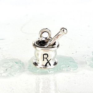 May include: Silver charm of a mortar and pestle with an Rx symbol. The charm is a small, detailed representation of a traditional pharmacy symbol.
