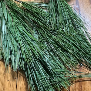May include: A close-up of a bundle of green pine needles on a wooden surface.