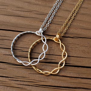 May include: Two intertwined silver and gold necklaces with circular pendant designs. The necklaces are on a wooden surface.